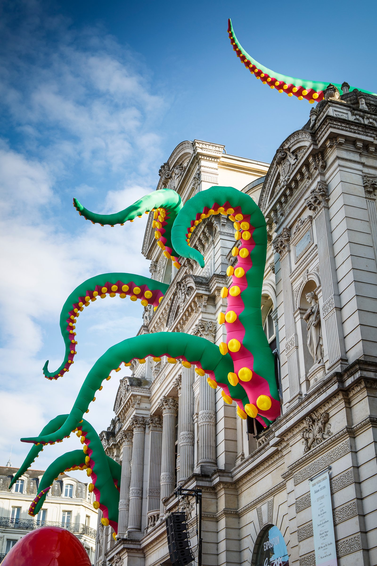 Large green and yellow octopus tentacles swarm out of the windows of a large stone building