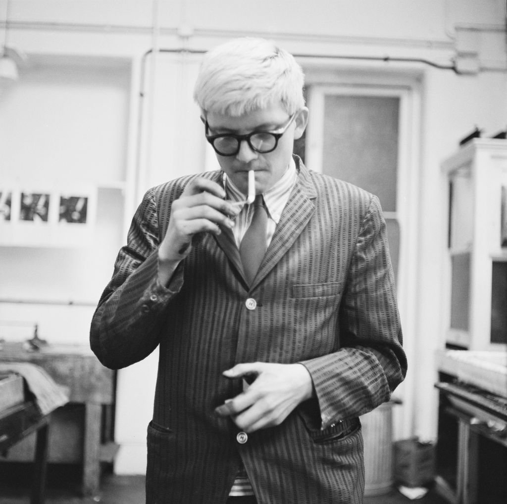 A black and white photo of a man in a suit and glasses lighting a cigarette.