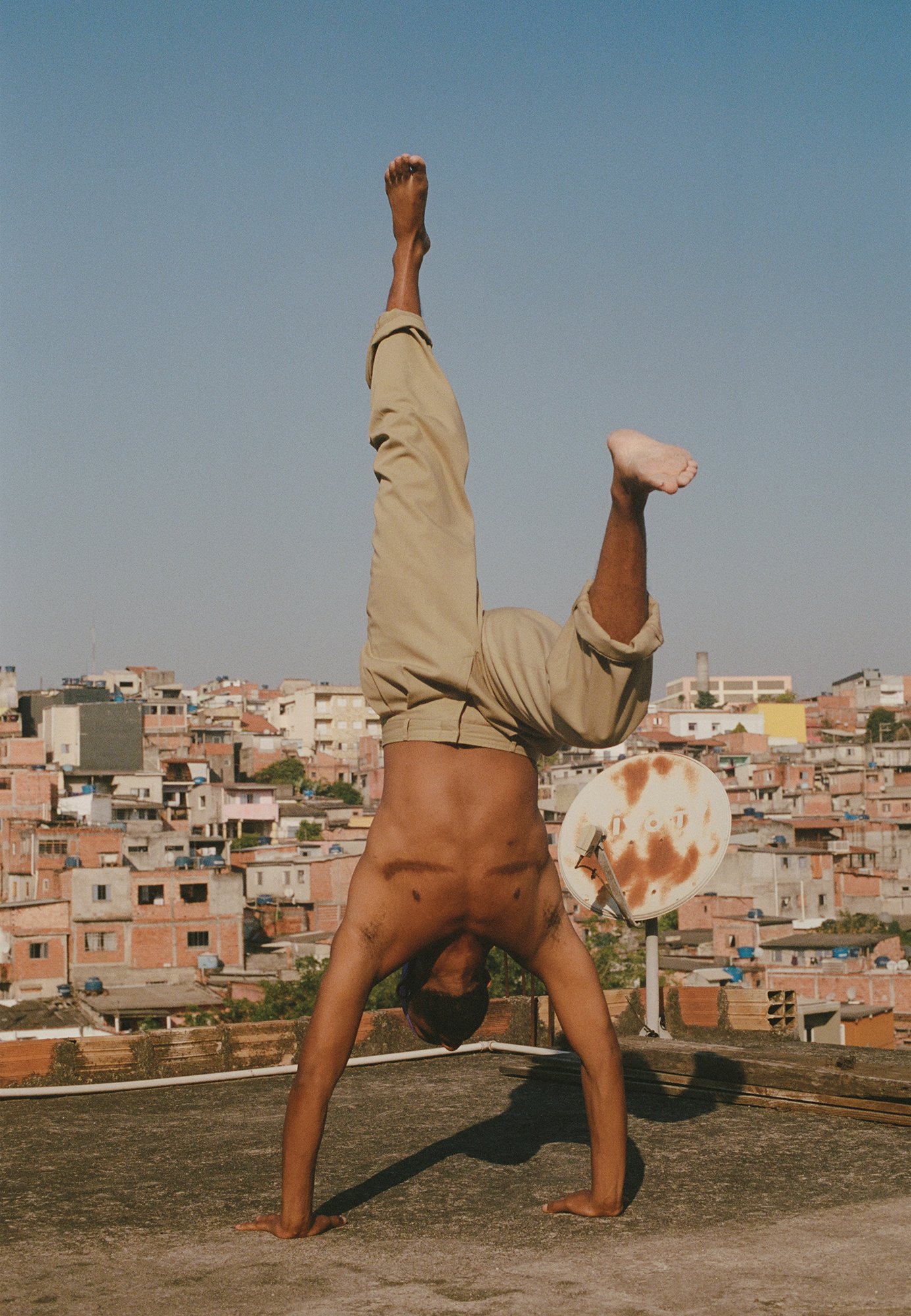 A photograph depicting person with scars on his pectoral muscles in the middle of a handstand, with Sao Paulo visible behind him.