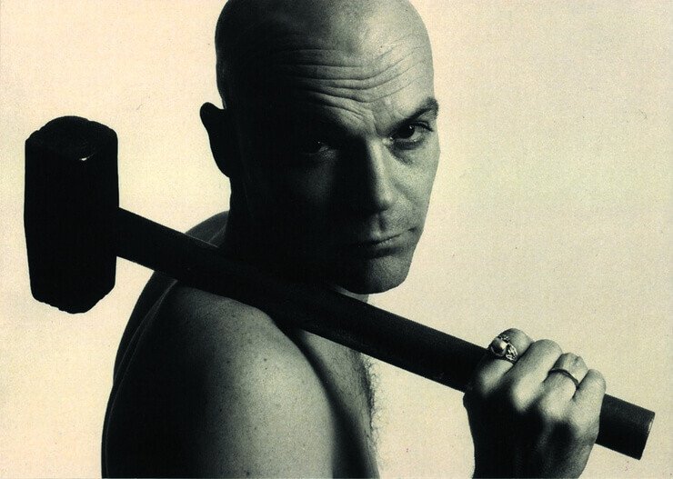 Black and white photo of shirtless man posing with hammer 